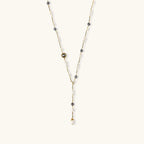 Y-shaped gold-plated necklace with white and gray freshwater pearls on cream background, showing adjustable drop design.